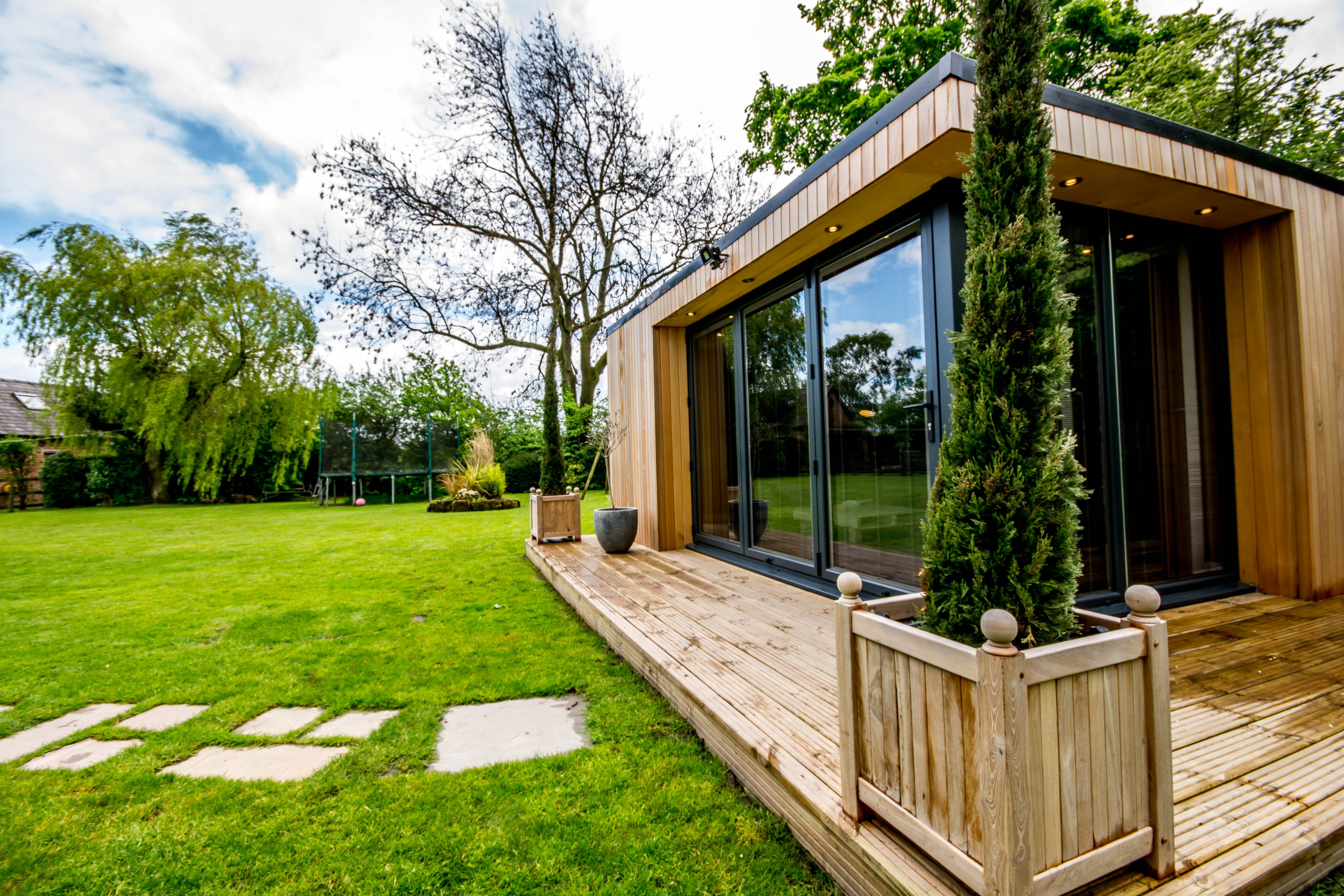 Modern granny annexe with large windows in lush garden setting.