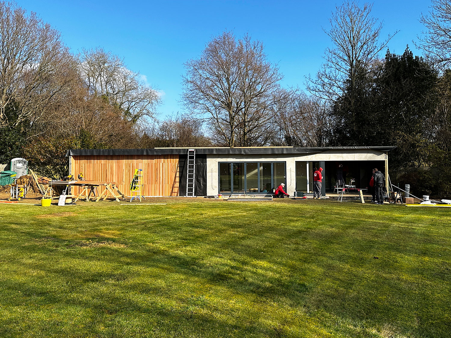 Workers construct modern granny annexe in spacious garden.